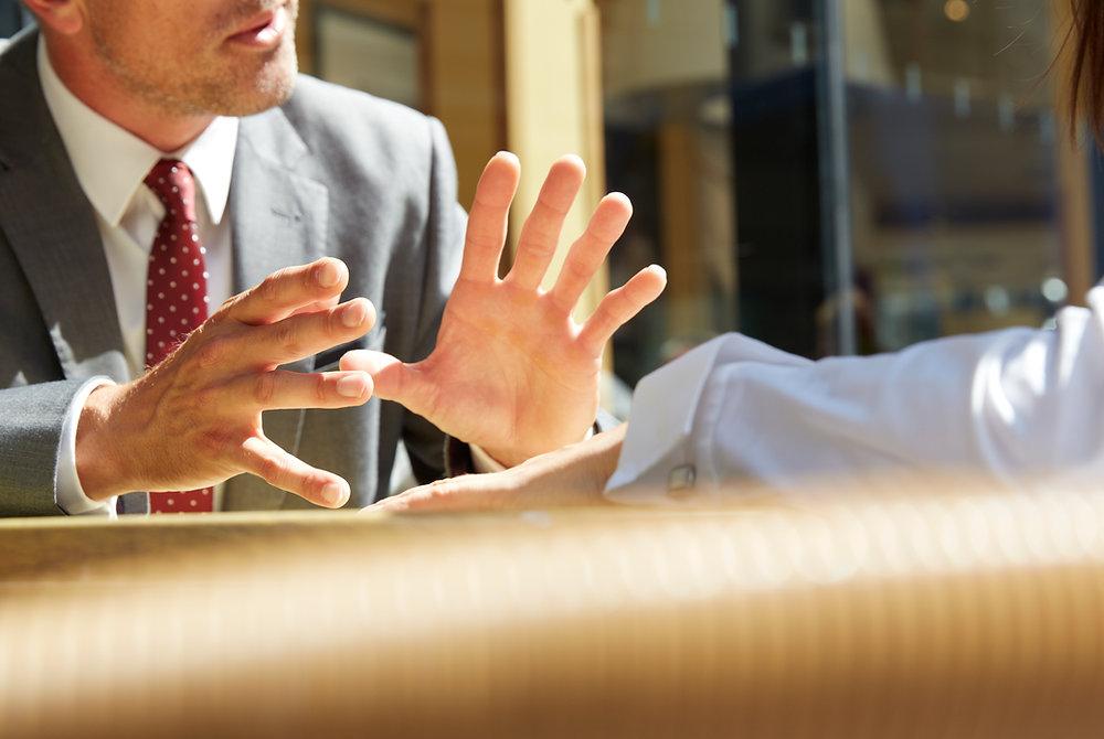 Syracuse family offense attorney gestures emphatically during conversation in a sunlit indoor setting with reflective windows.