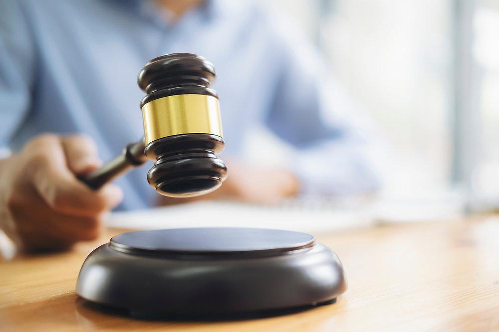 Close-up of a gavel striking a sound block. Syracuse CPS attorney is blurred in the background, creating a focused, decisive mood.